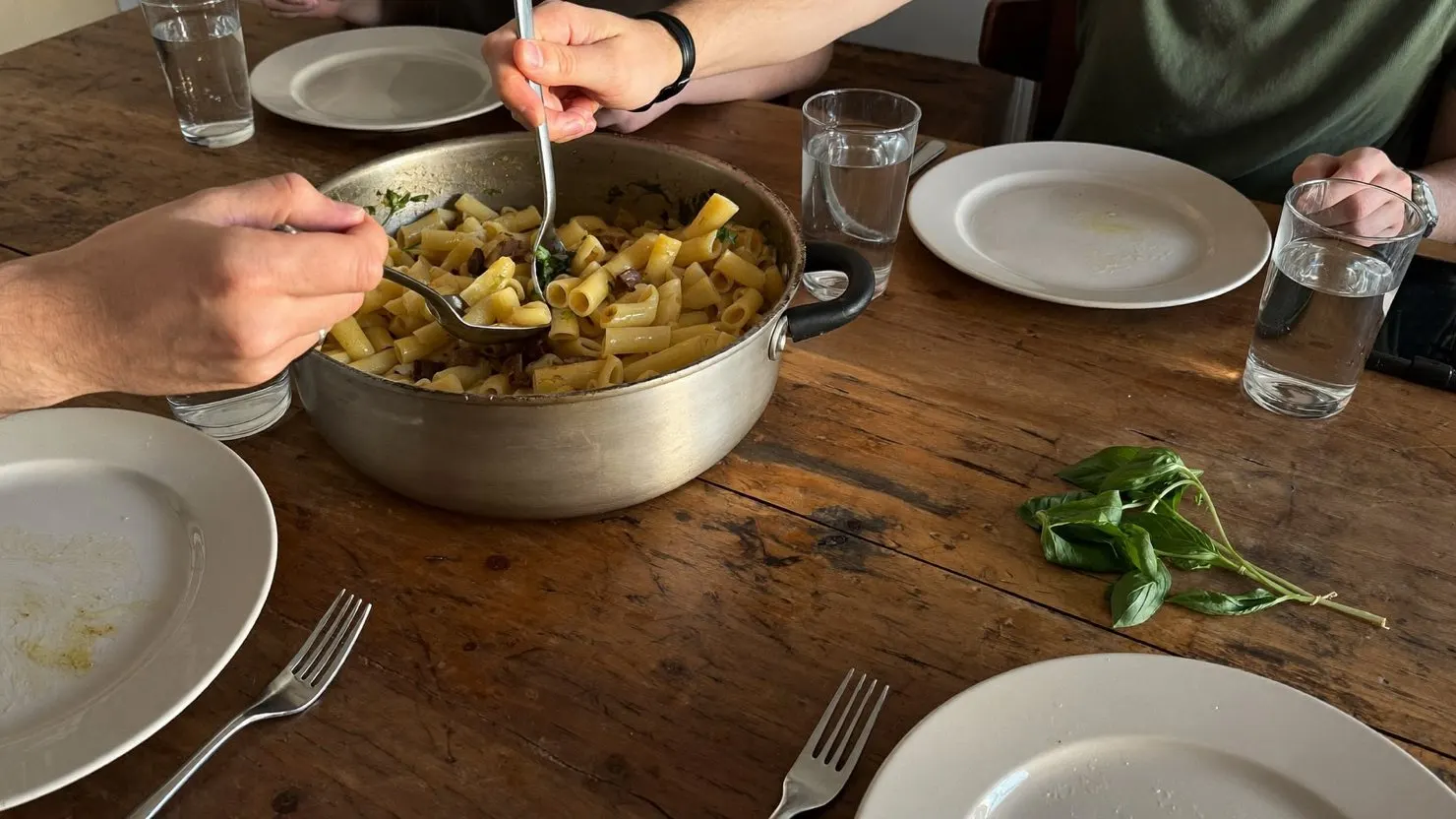 Des colocataires partagent une casserole de pâtes autour d'une table en bois usée, dans la cuisine d'une maison étudiante néerlandaise
