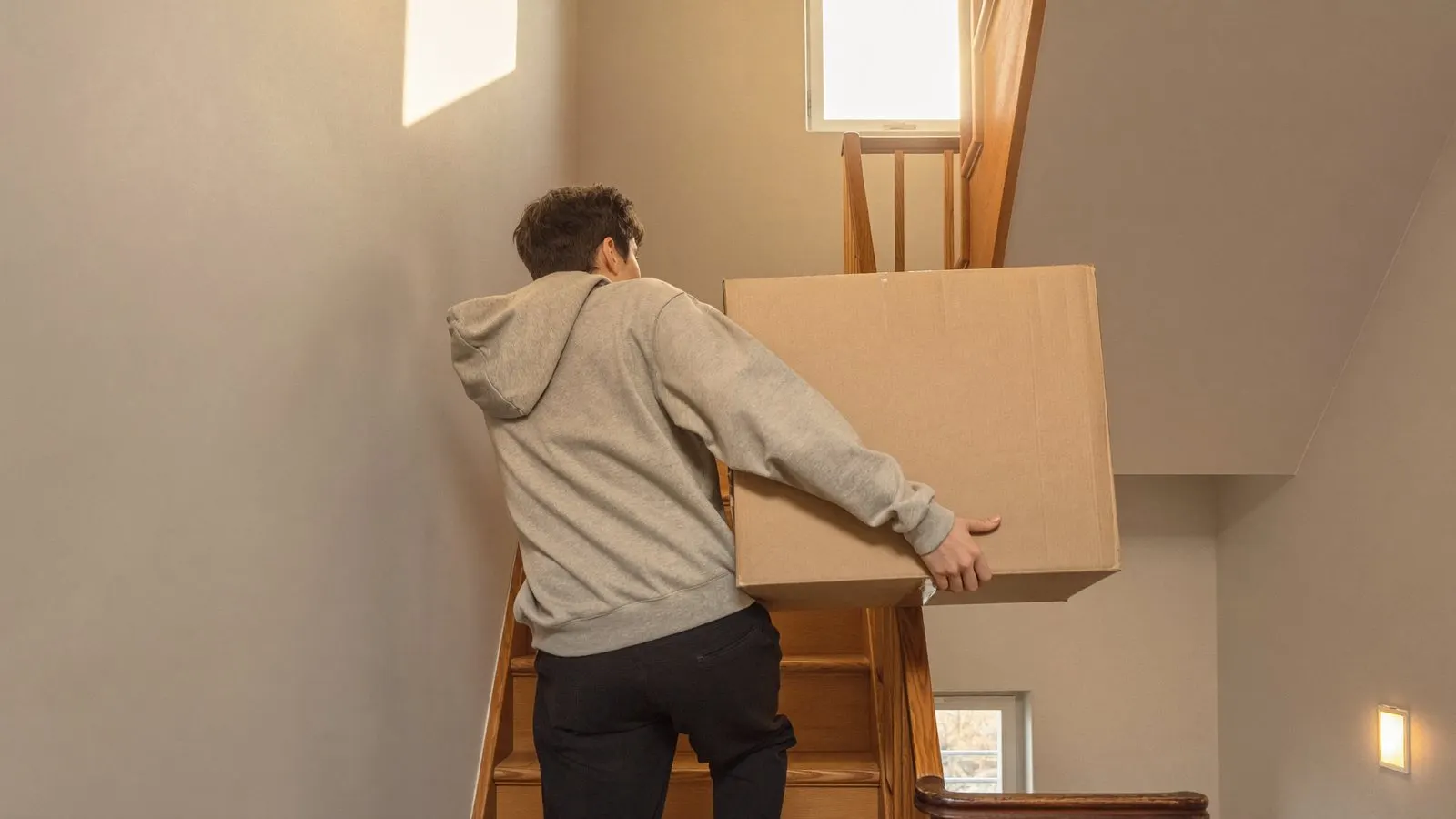 Un étudiant monte un carton de déménagement dans un escalier néerlandais raide et étroit, le jour de l'emménagement