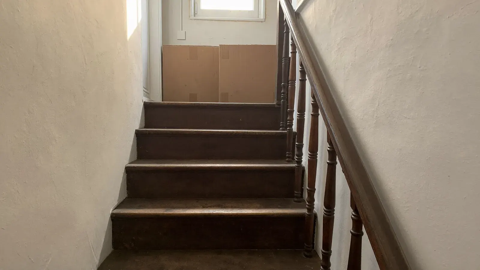 Eine schmale, alte niederländische Treppe führt zu einem Treppenabsatz mit zwei unbeschrifteten Umzugskartons unter einem kleinen Fenster